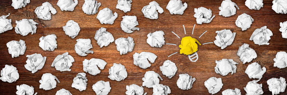 wide panorama wooden desktop with many paper balls and lightbulb idea symbol / holz schreibtisch mit Papierknäuel und Glühbirne Idee Symbol panorama banner format